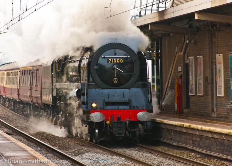 a locomotive is going down the tracks by a train station