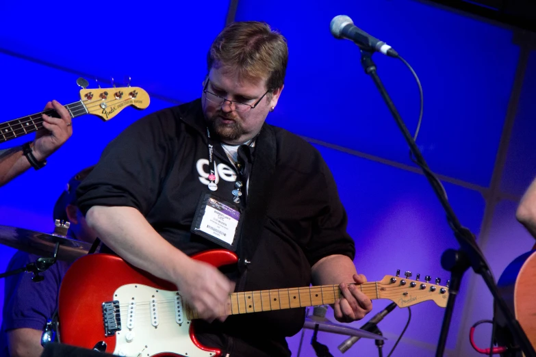 three men with microphones on and one playing the guitar