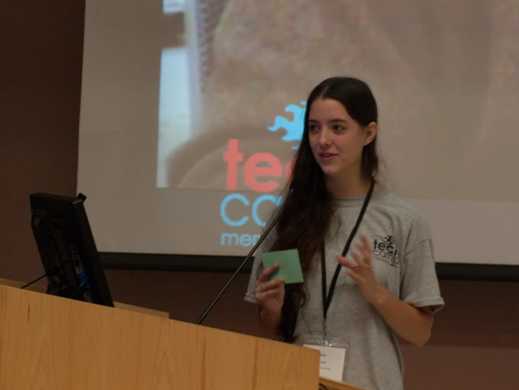 a woman is speaking at a podium in front of a projected screen