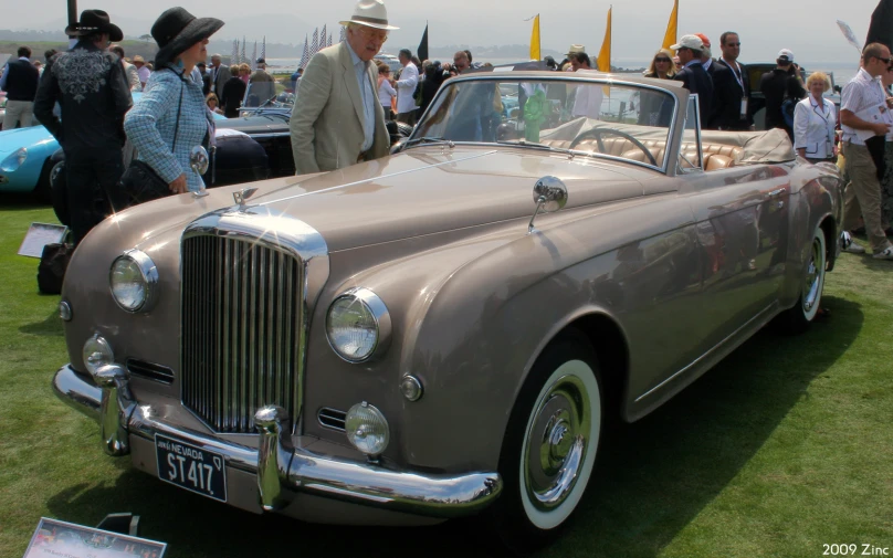 two men talking to each other while standing next to an old classic car