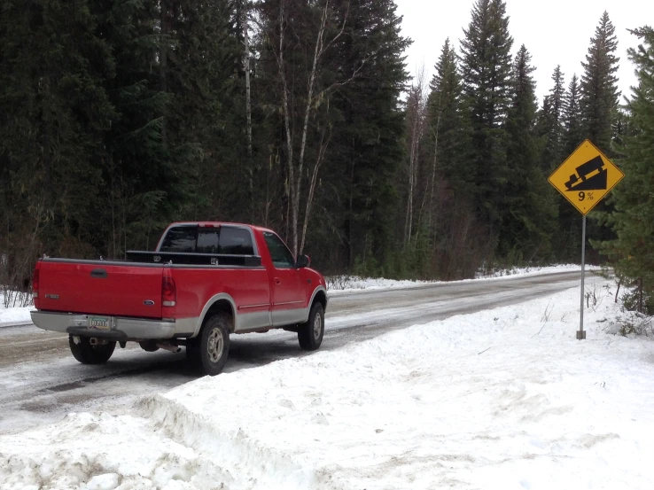 a red truck is on the snow and beside a road sign