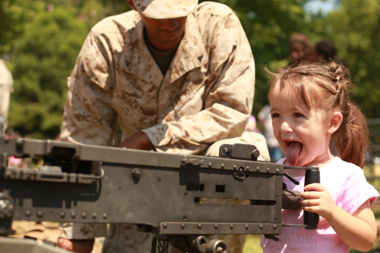 a little girl has her tongue out in front of an army machine