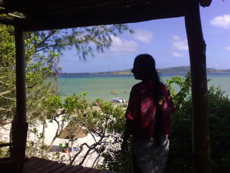 a person in a red and white shirt standing on the porch next to the water