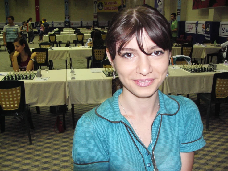 a lady wearing a turquoise shirt stands in the middle of tables