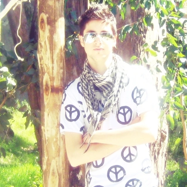 a man in peace signs t - shirt stands with arms crossed next to a tree