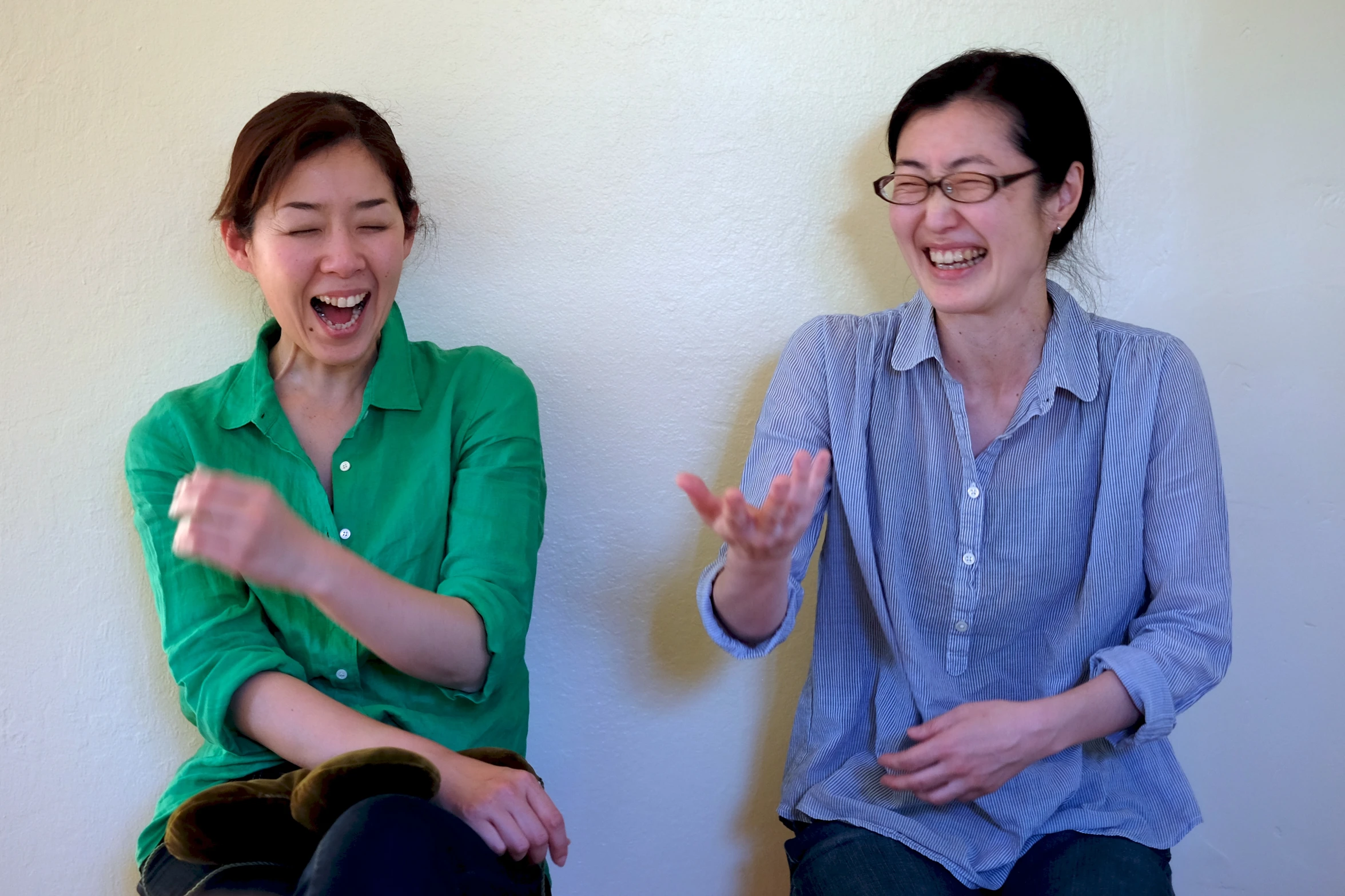 two woman sitting next to each other in front of a wall