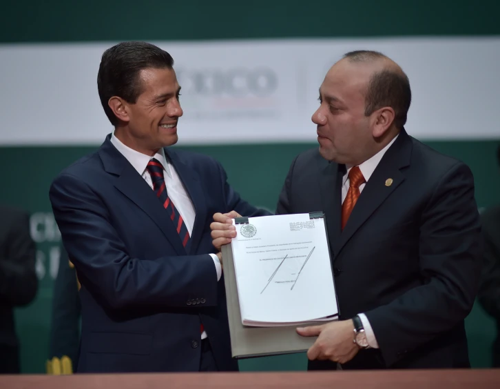 two men smile while one holds his paper in his hand