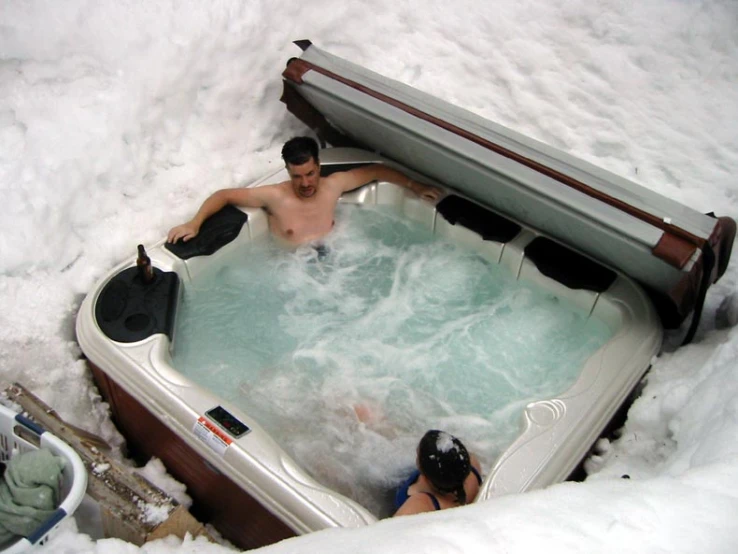 a man and woman in a  tub with snow on the ground