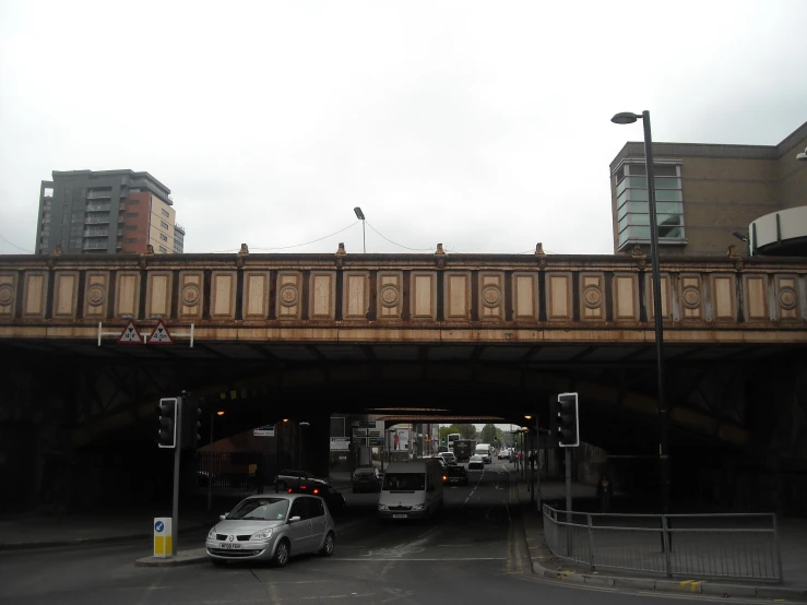 an intersection on a busy road with cars passing underneath a bridge