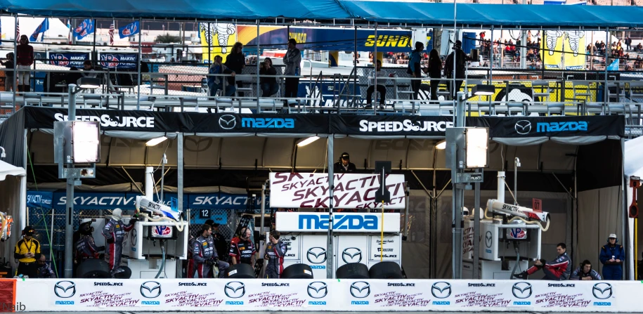 an audience watches as an event takes place in front of a fence