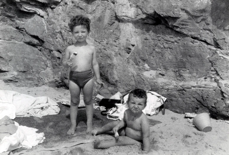 two boys on the beach near a rocky wall