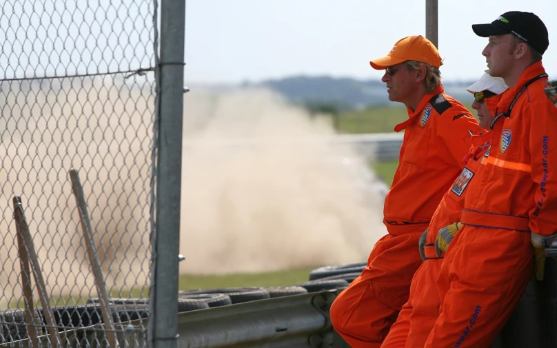 two men stand on the side of a fence and watch as dirt is spray