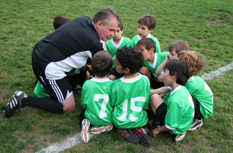 there are boys and a coach in a soccer team huddled together