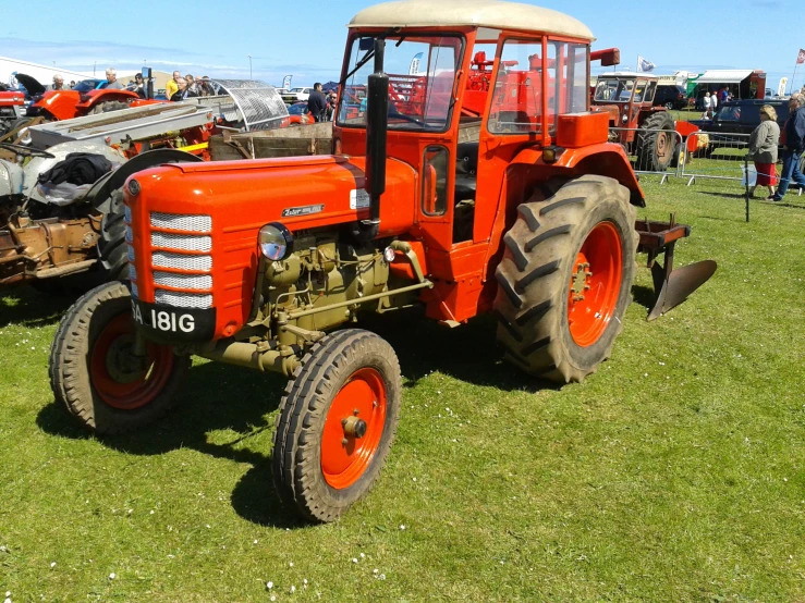 an old orange tractor parked on top of a green field