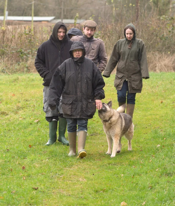 a group of people are walking down the grass with their dog