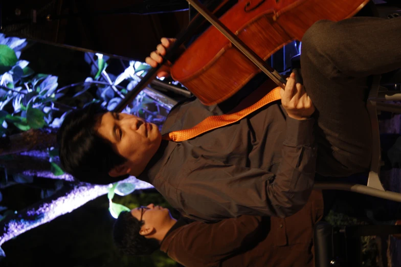 an asian man sitting in a chair playing a cello