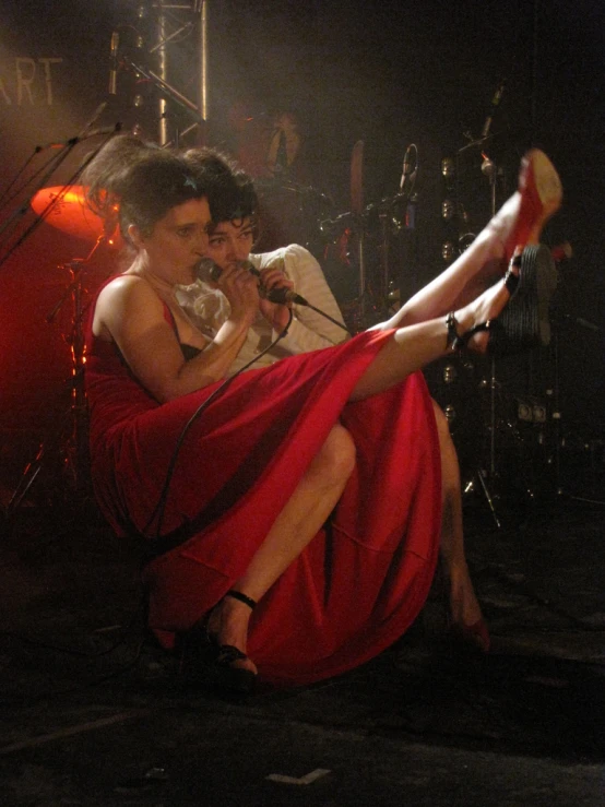 a woman wearing a red dress with her legs hanging out and a man wearing white shirt