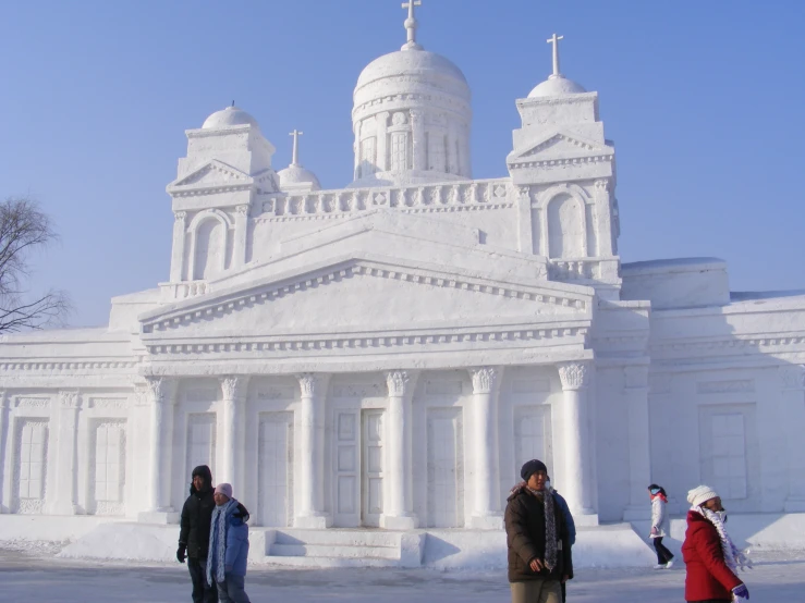 people stand outside of a church covered in snow