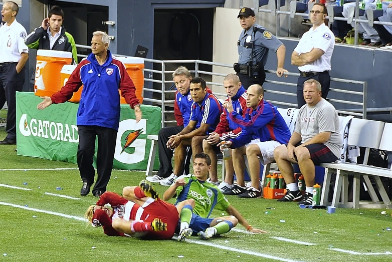 a soccer player lies on the field and a team member stands beside him