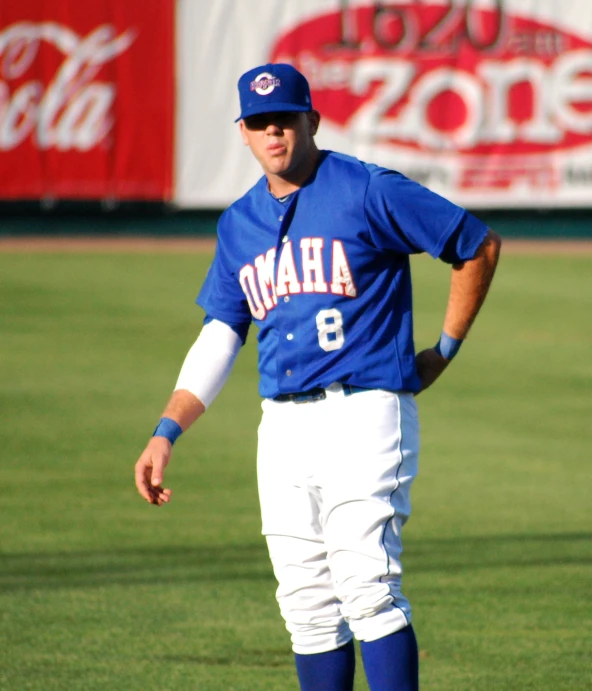 a man with a hat and sunglasses stands on a baseball field