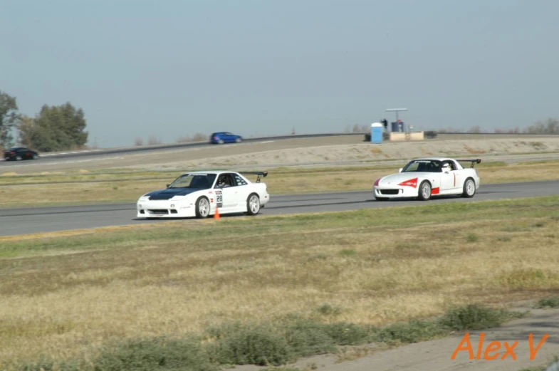 two small white sports cars racing on an asphalt race track