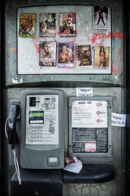 a public payphone on the side of a wall with posters of different women