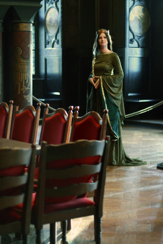 the woman dressed in green with yellow is standing in a room full of red chairs