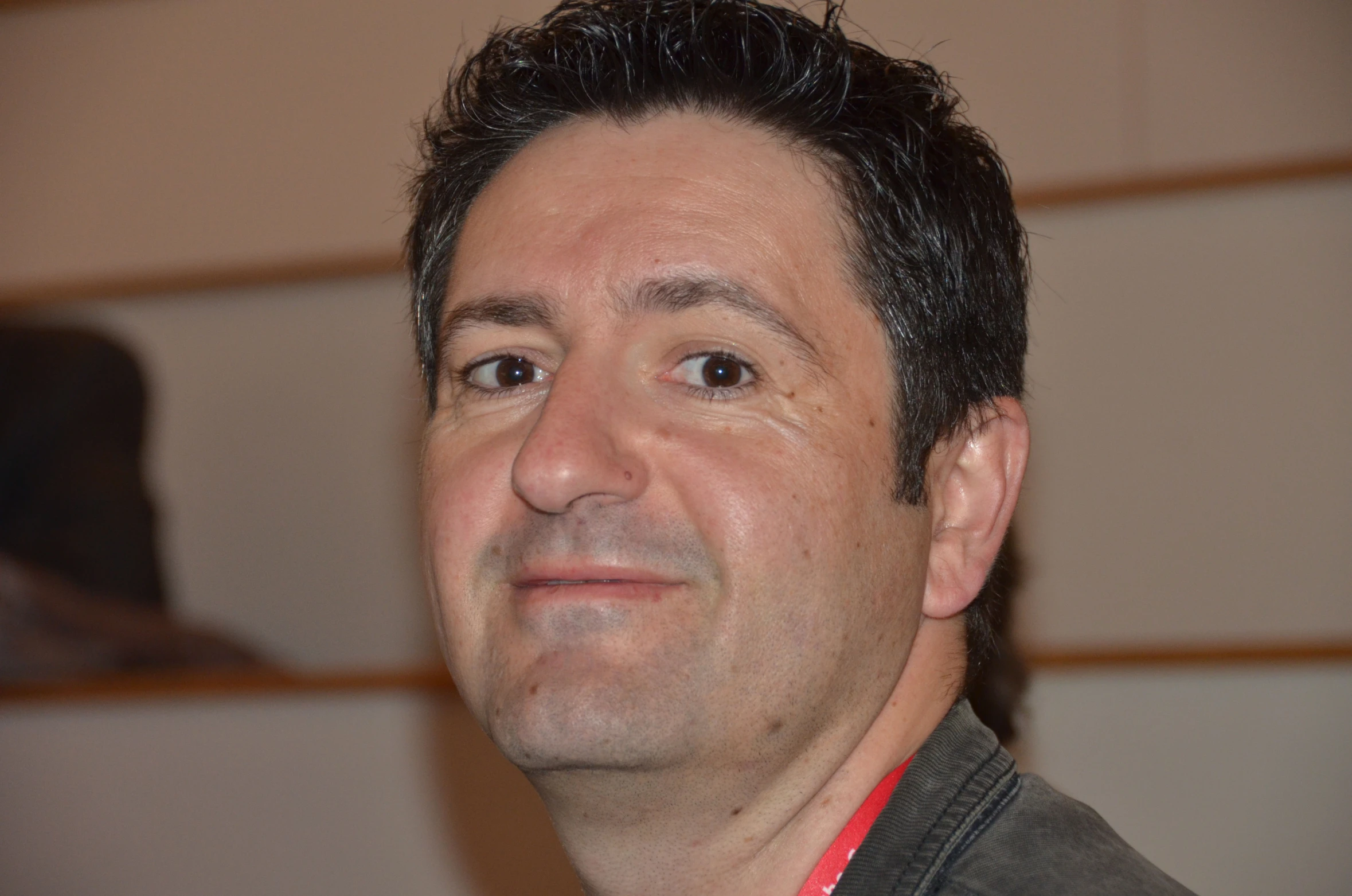 a man in gray shirt with black hair and a smile