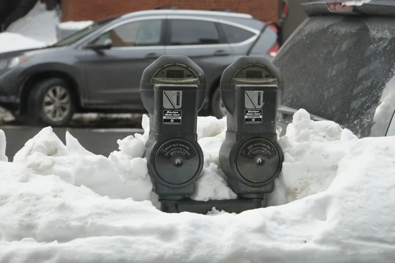 two parking meters stand in a pile of snow