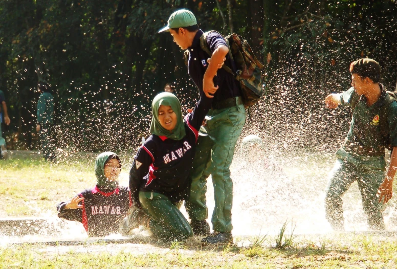 two s playing baseball in water as adults watch