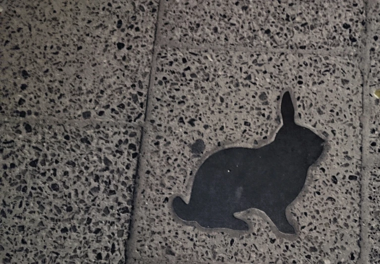 a black rabbit silhouette on a sidewalk next to a street light
