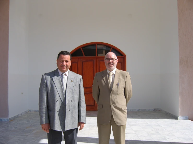 two men in suits stand outside of a building