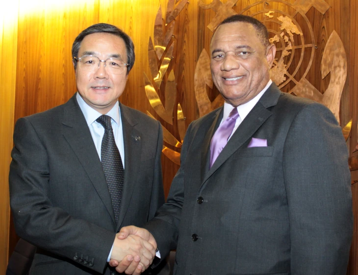 two asian men in suits shake hands in front of the clock