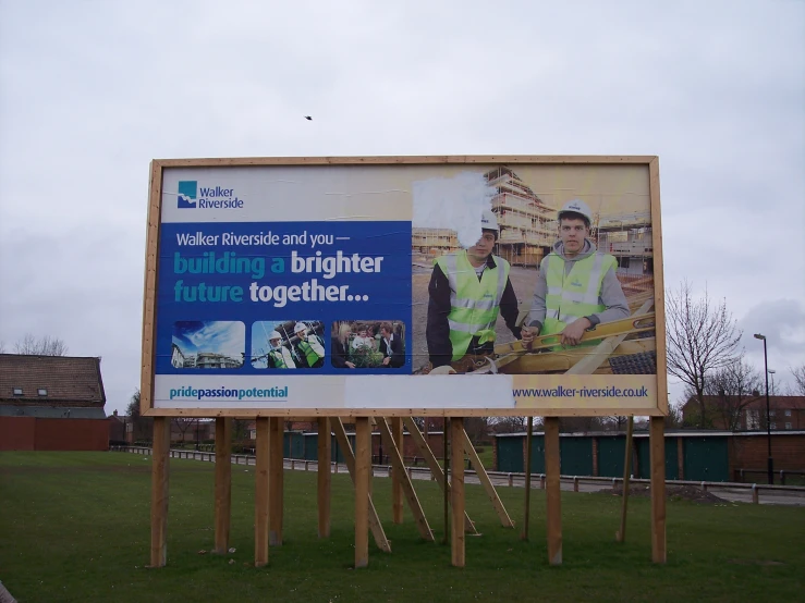 a billboard is in a grassy field as construction workers stand around