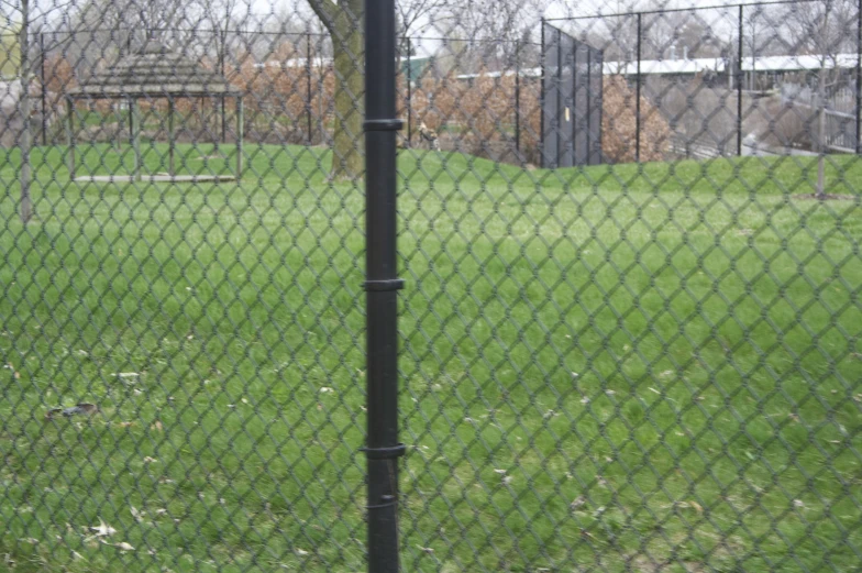 a man stands behind a fence as he swings a baseball bat