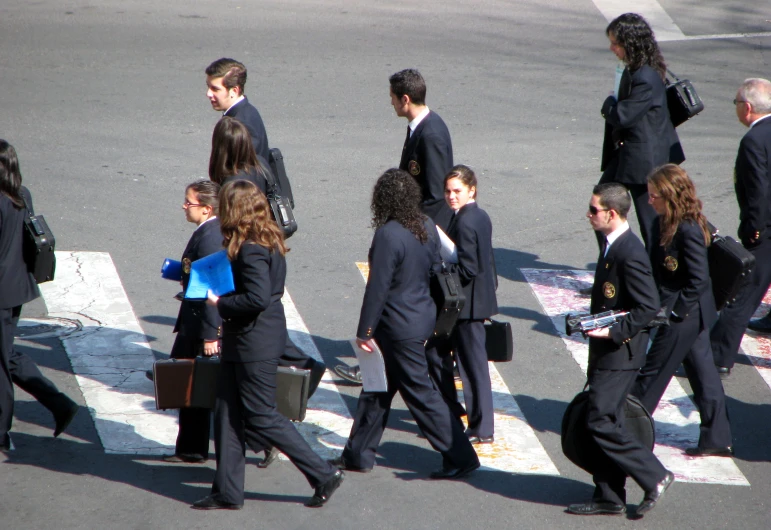 group of people dressed in suits cross a city street