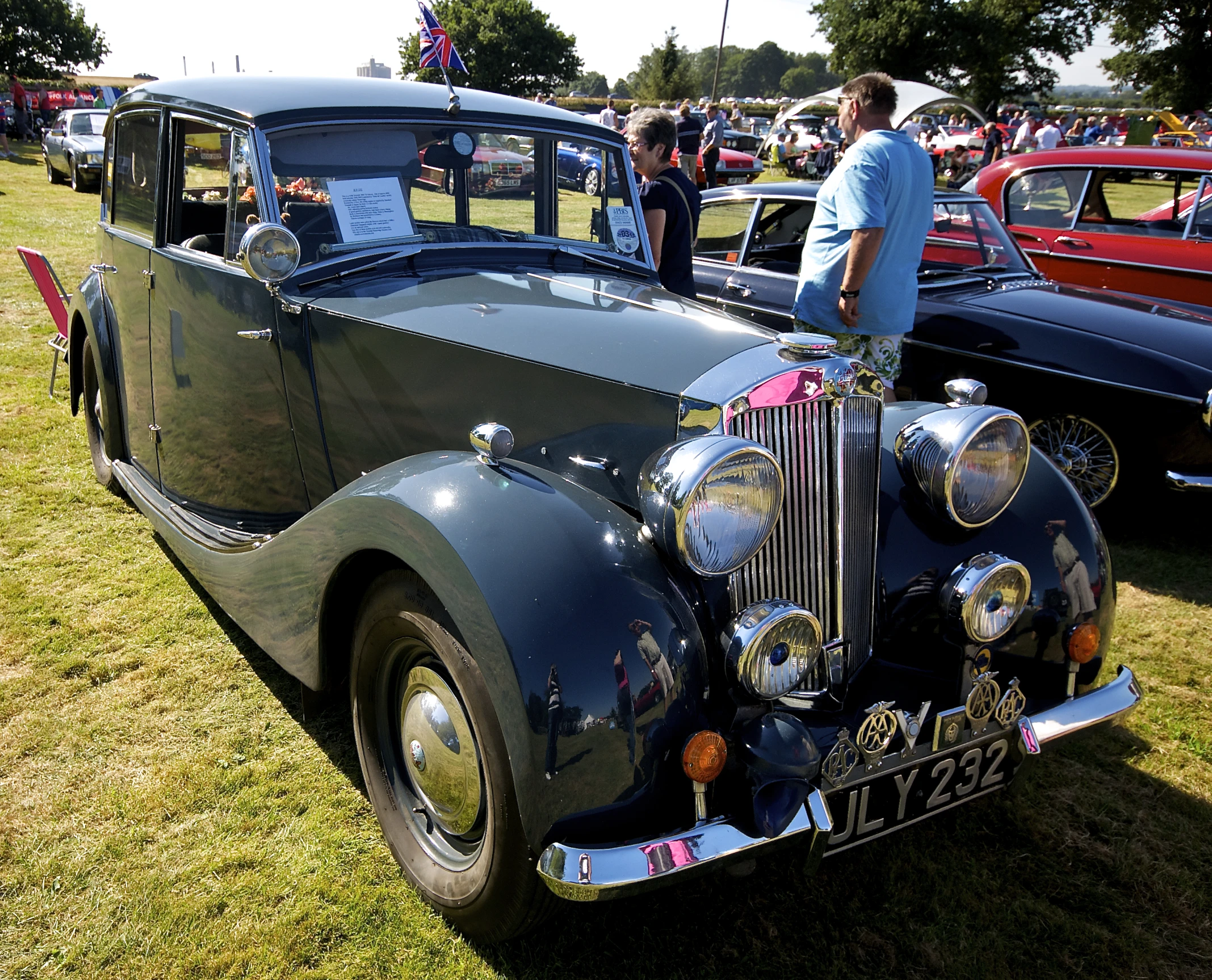 a classic car parked on the side of a grass covered field