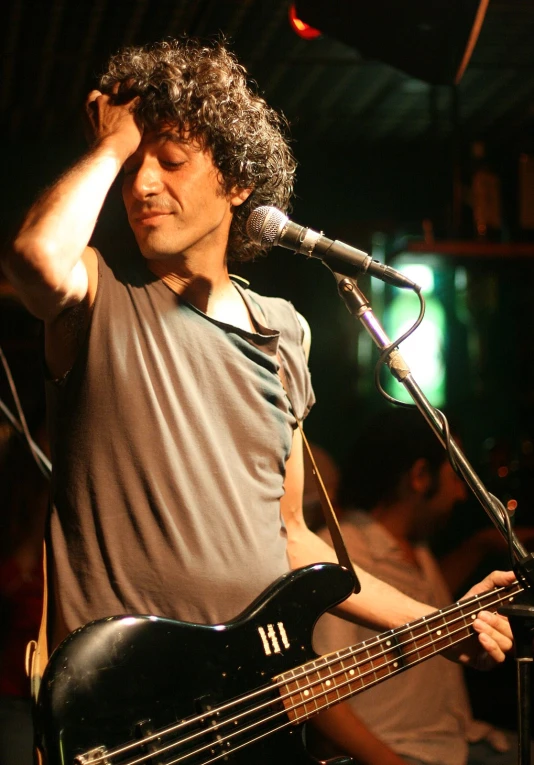 a man with a gray shirt holding a black bass guitar