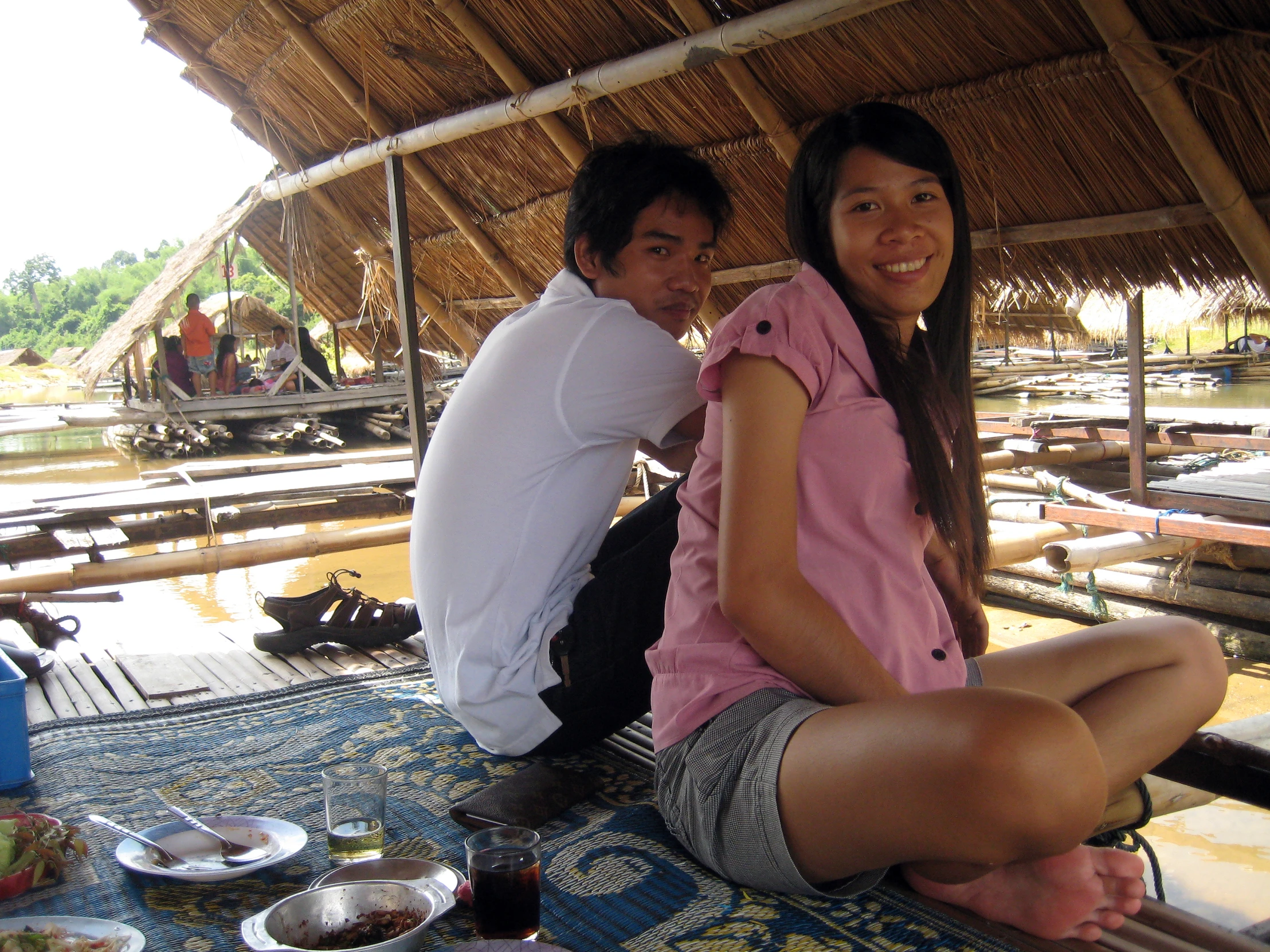 man and woman sitting on the ground under a straw hut