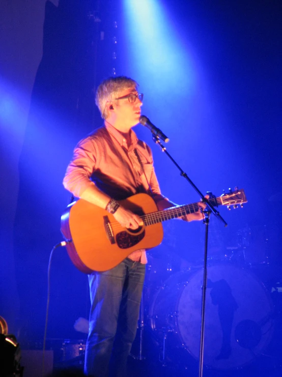 man in orange shirt singing and playing guitar