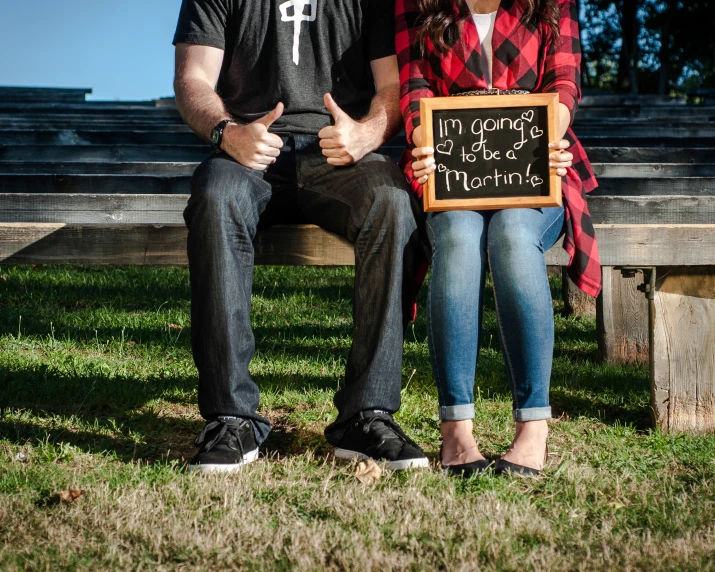 two people sitting on a park bench with a chalk board