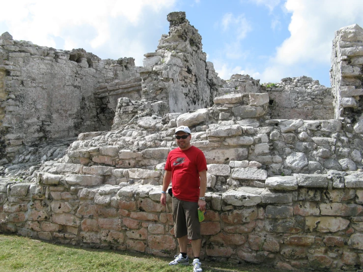 a man in a red shirt and sunglasses standing by a stone structure