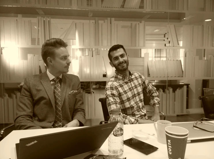 two men sitting at a desk working on a laptop