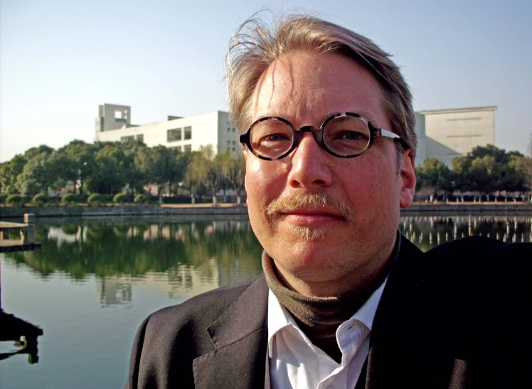 man wearing glasses and a suit in front of a lake