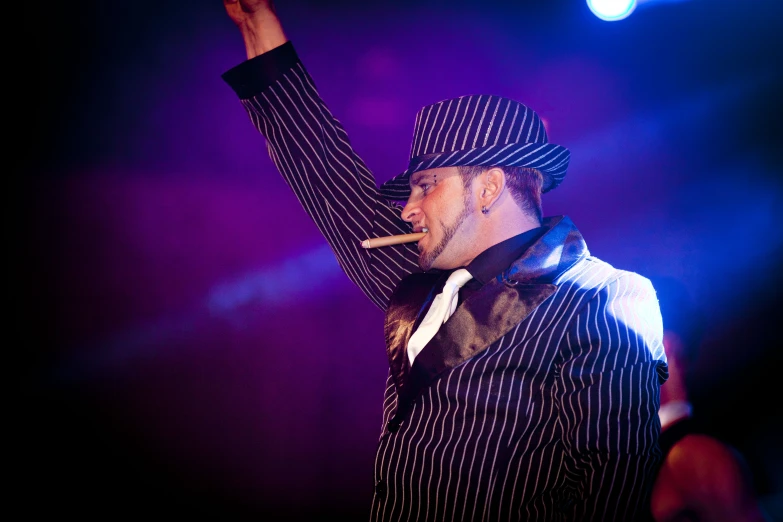 a man with his hands up in a hat and tie, holding up a cigarette