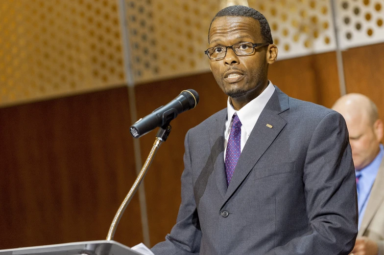 an african american man speaking at a podium with other men