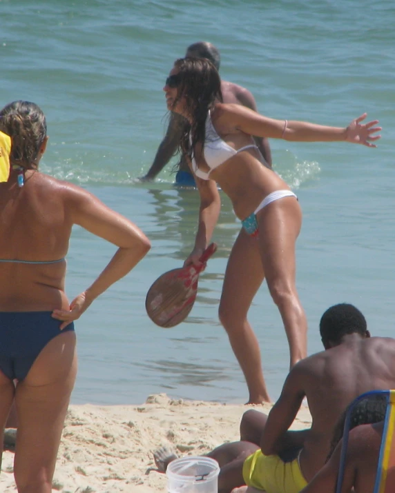 two women playing frisbee on a beach with others