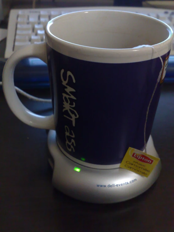 a coffee cup with a sticker on it sitting in front of a keyboard