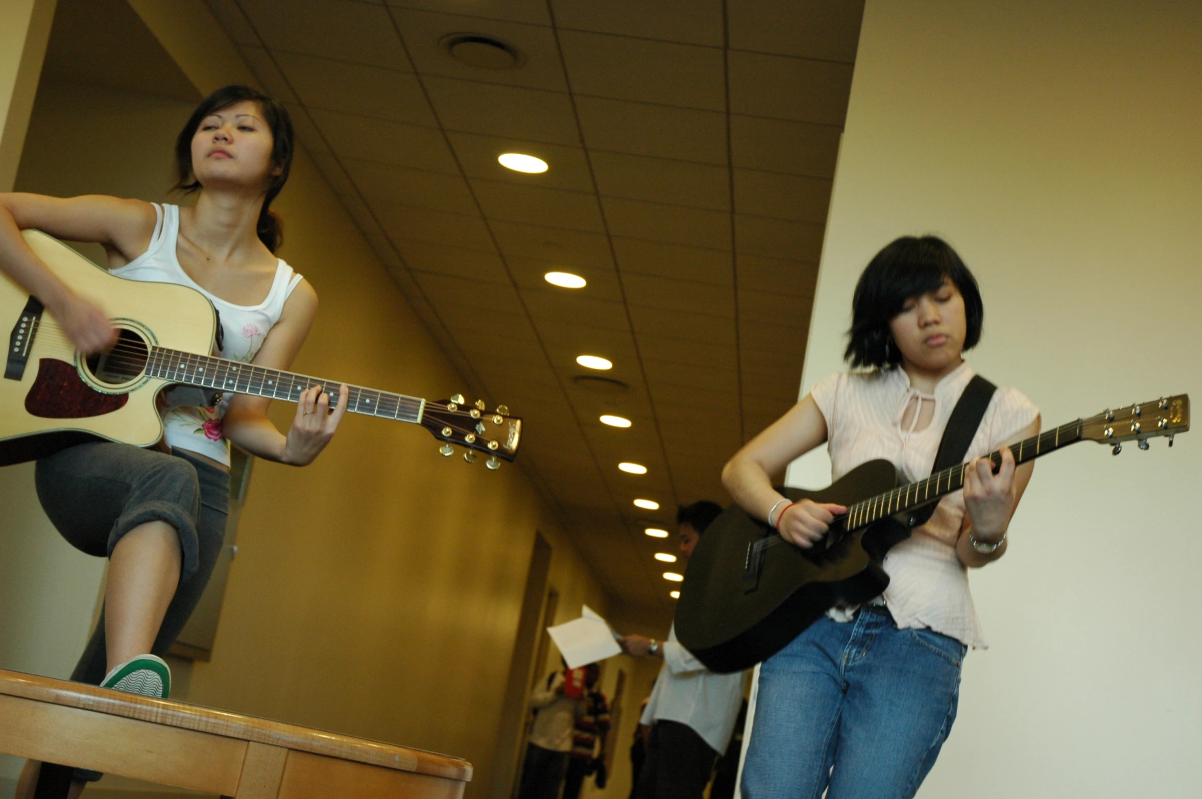two girls playing guitars in a hallway together