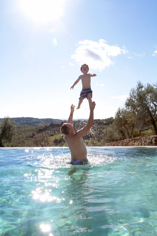 a man balances his child over his head in a pool of water